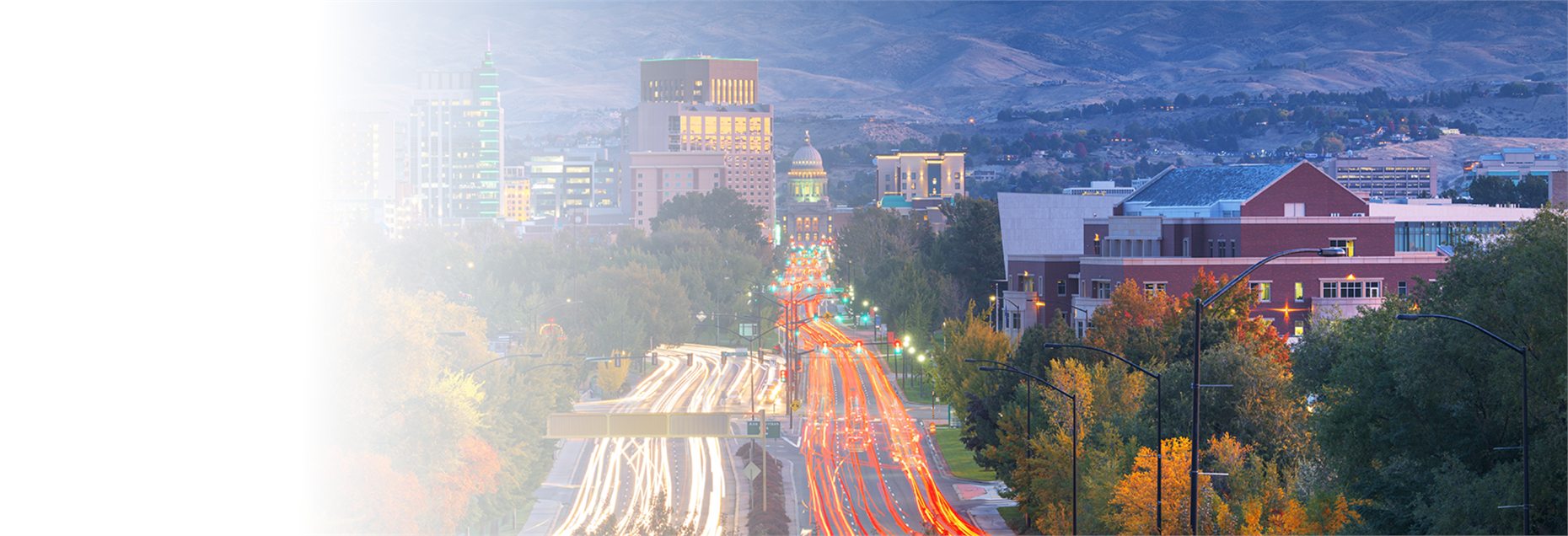 Downtown Boise at dusk: Capitol Boulevard's traffic streaming toward the Idaho State Capitol, with the foothills behind
