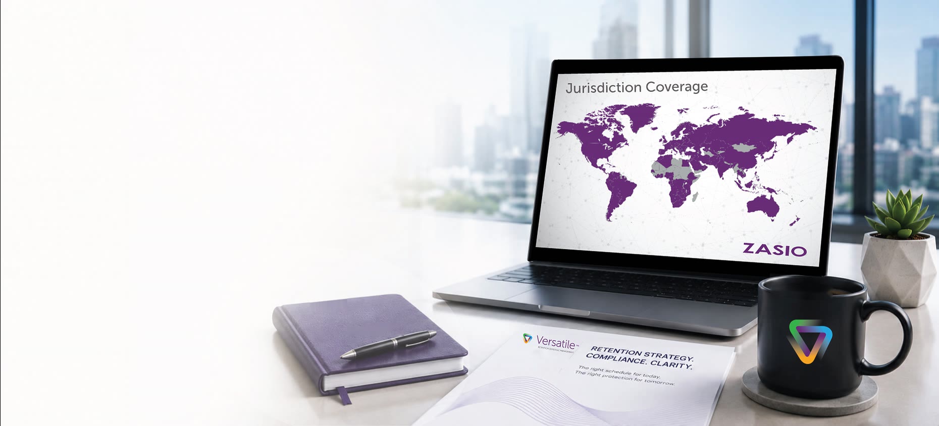 A laptop on a desk showing a Zasio jurisdiction coverage world map, beside a notebook, a Versatile Retention Schedule Management brochure, and a mug with the Versatile mark, city towers through the window