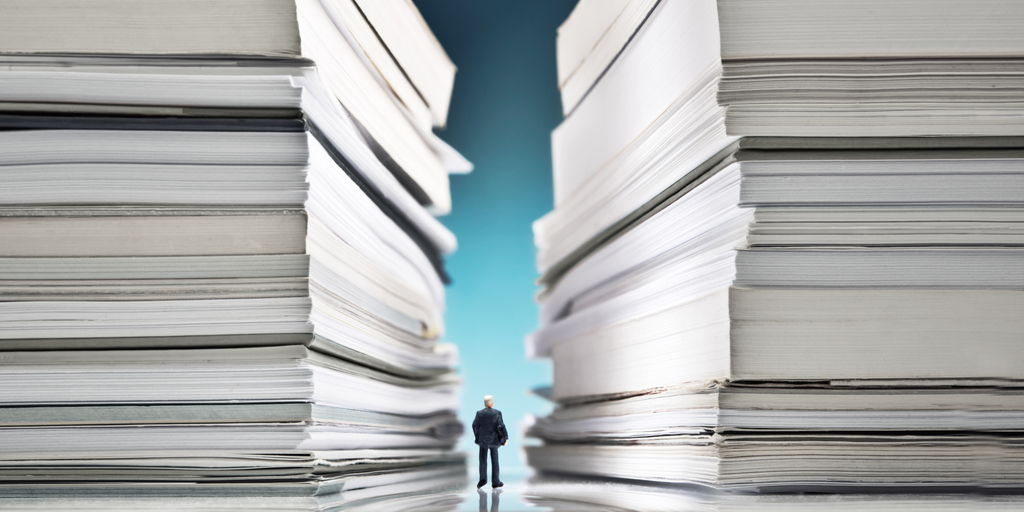 miniature man between two large stacks of files