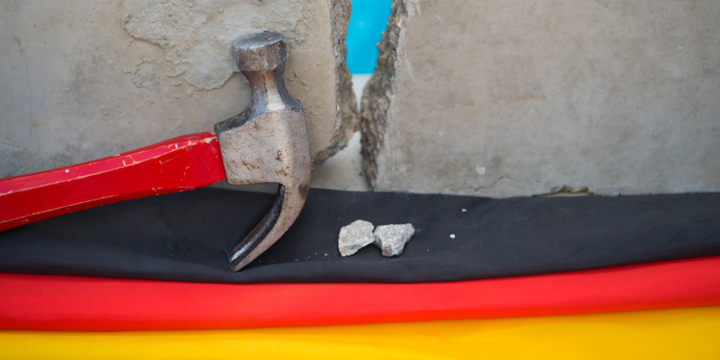 closeup German flag beneath hammer and broken wall