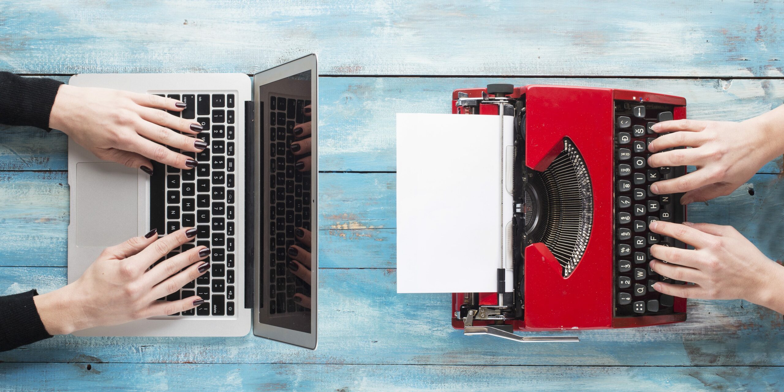 Ariel view of red typewriter and MacBook on blue wood desk
